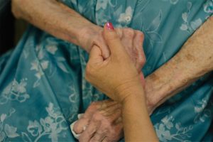 a woman holds the hand of a nurse at a skilled nursing facility