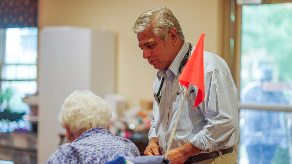 A man pushes a woman in a wheel chair at a skilled nursing facility